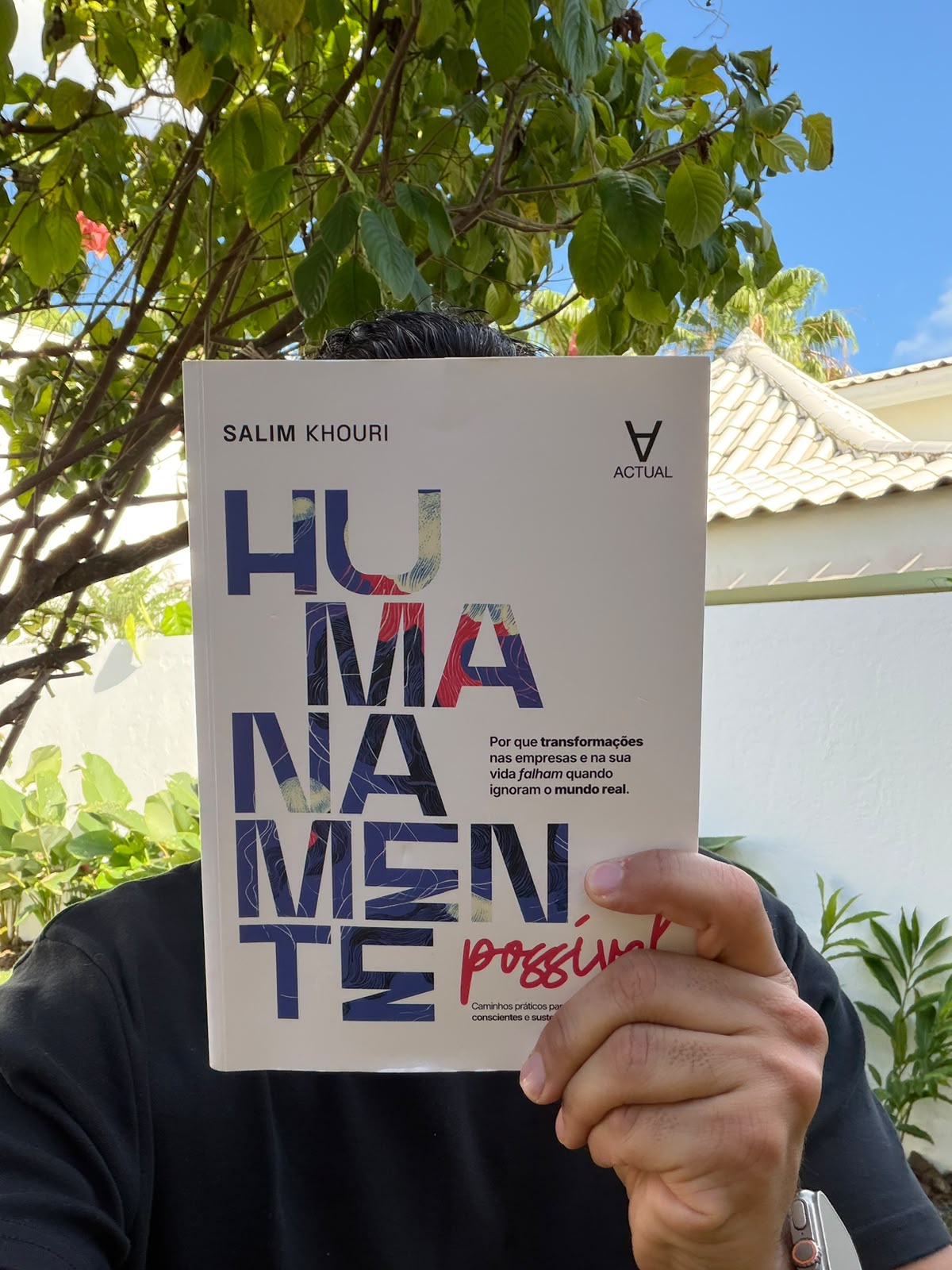 Salim Khouri segurando o livro Humanamente Possível em frente ao rosto, em ambiente externo.